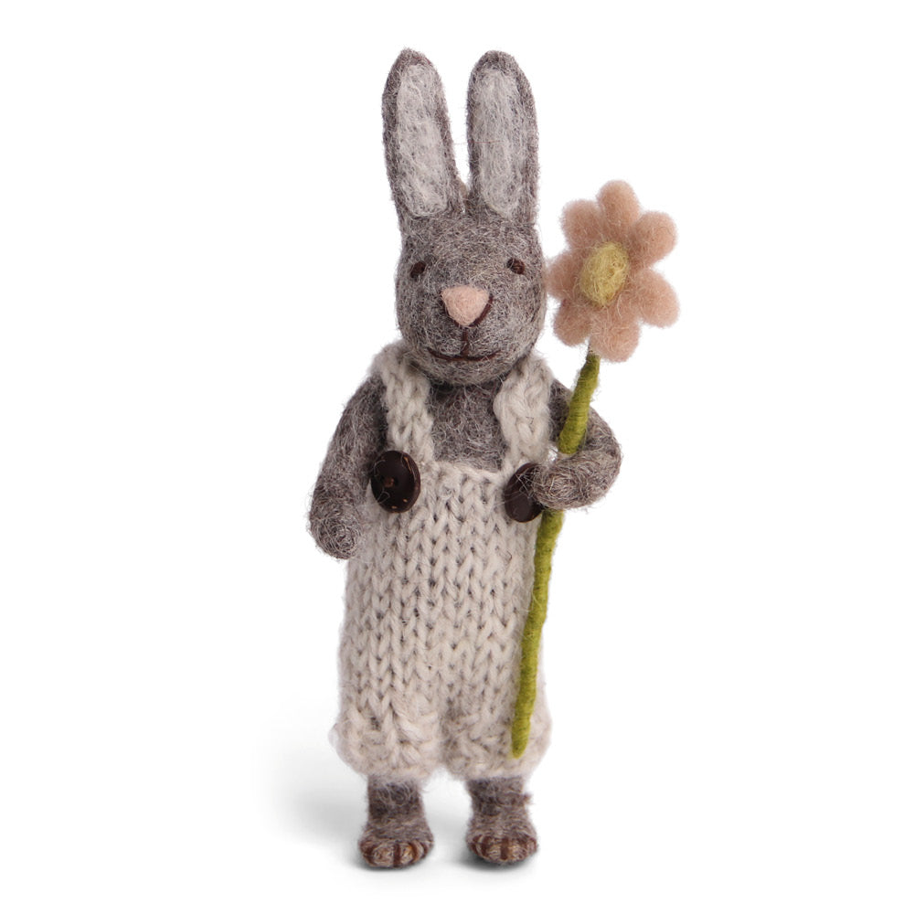 Ein niedliches Filzkaninchen in gestrickter Kleidung hält eine blassrosa Filzblume. Perfektes handgemachtes Osterdekor.