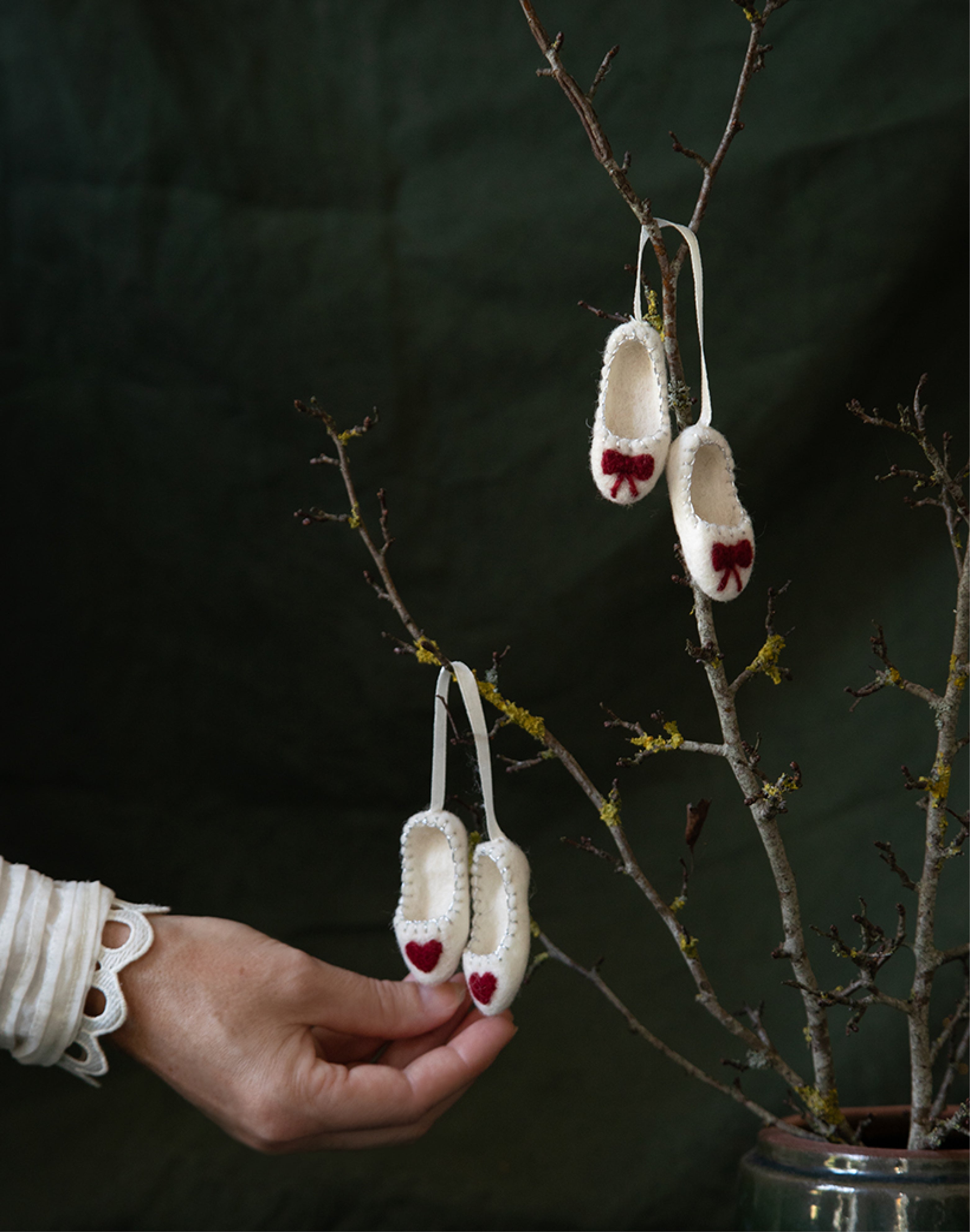 Weiße, handgefilzte Ballerina-Schuhe mit Schleife von Gry & Sif – festliche Filzanhänger an einem Ast dekoriert.