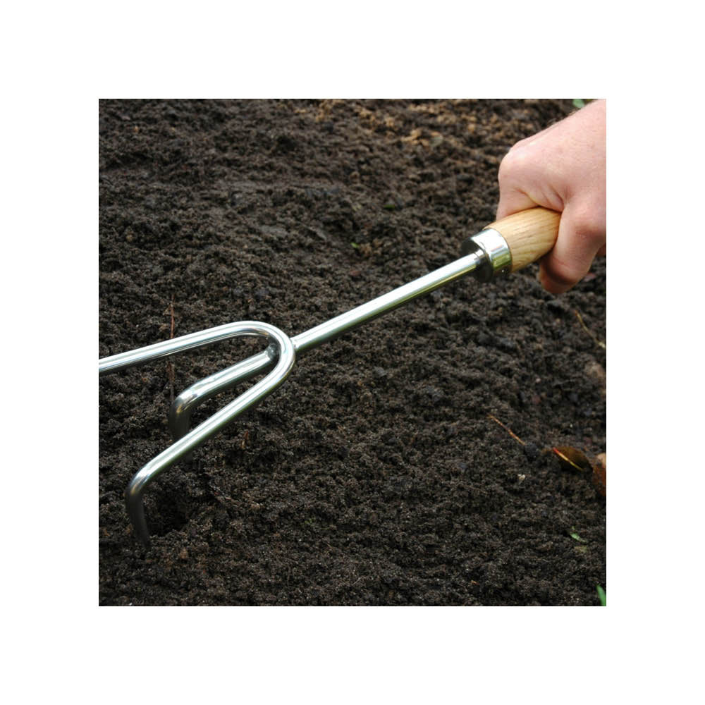 Handharke beim Lockern der Erde im Beet – Edelstahl-Gartenwerkzeug mit Holzgriff