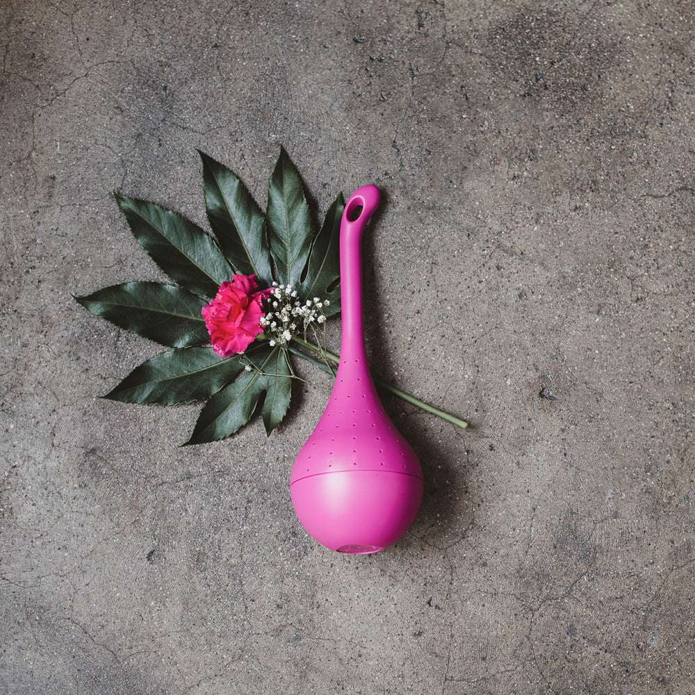 Schmetterlingsfutterstelle Belightful in Pink liegend auf Beton, dekoriert mit Blumen.