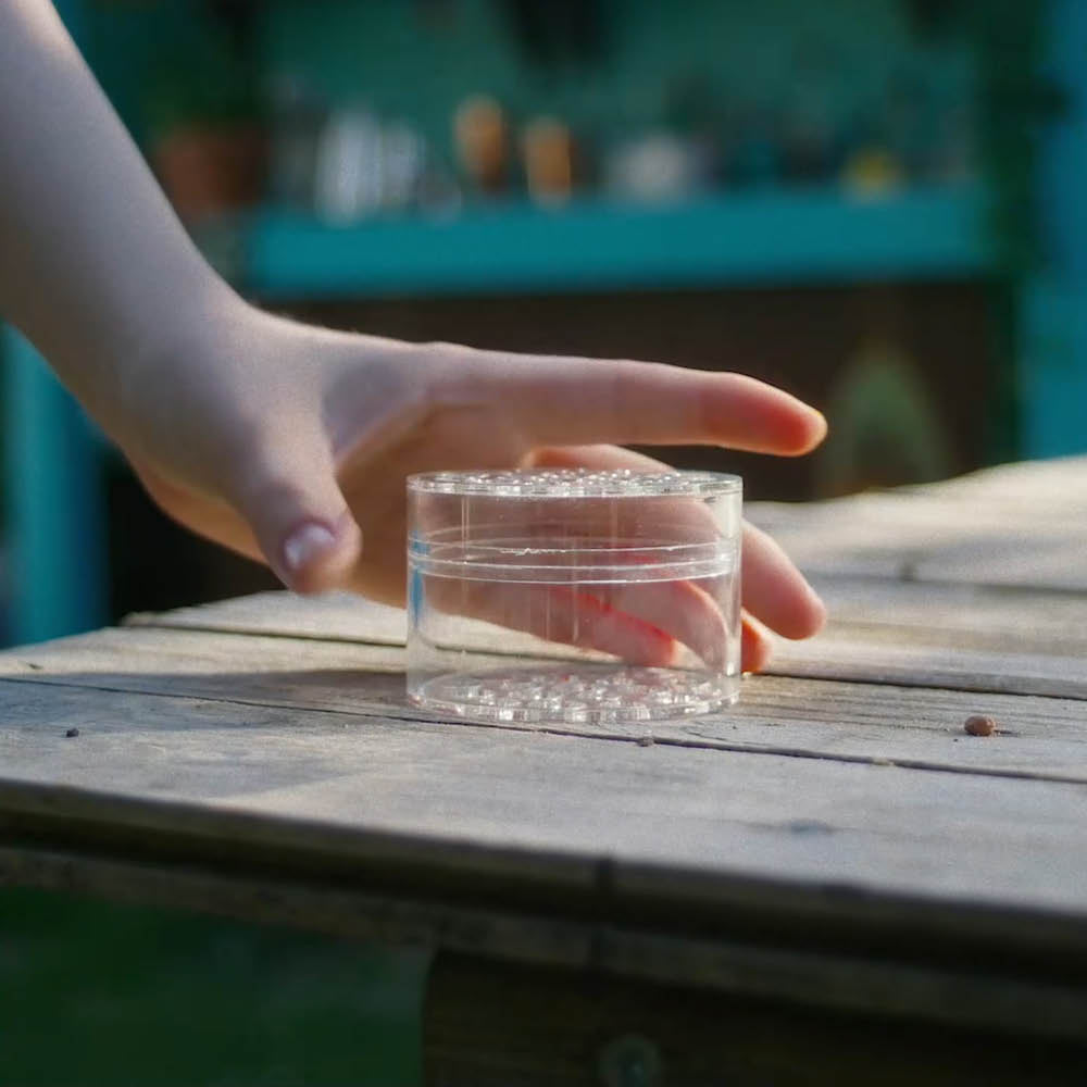 Hand legt das Hanataba „Crystal Clear“ auf einen Holztisch im Garten.