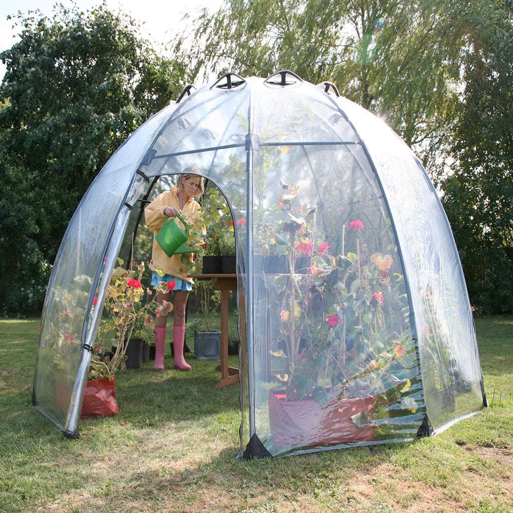 Eine Frau giesst Pflanzen im Haxnicks Sunbubble Gewächshaus 